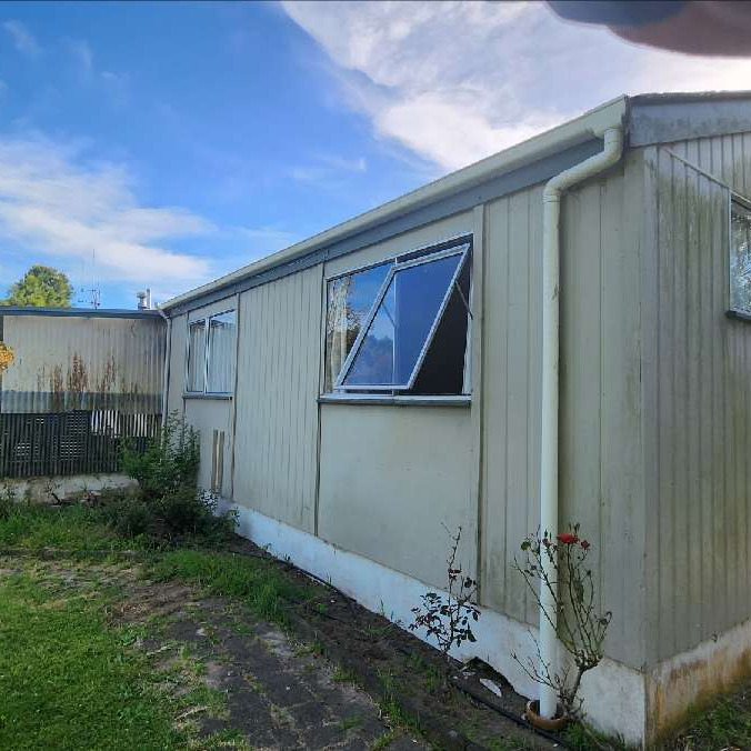 Weathered cream weatherboard home before ADCO Roofing's reclad and re-roof, with tired cladding, windows and spouting.