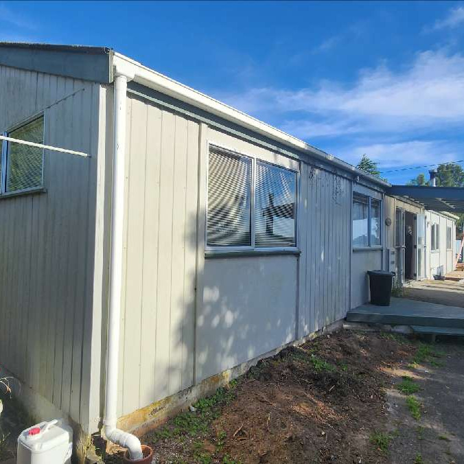 Side of the house showing pale, dated cladding before ADCO Roofing's Flaxpod reclad and re-roof.