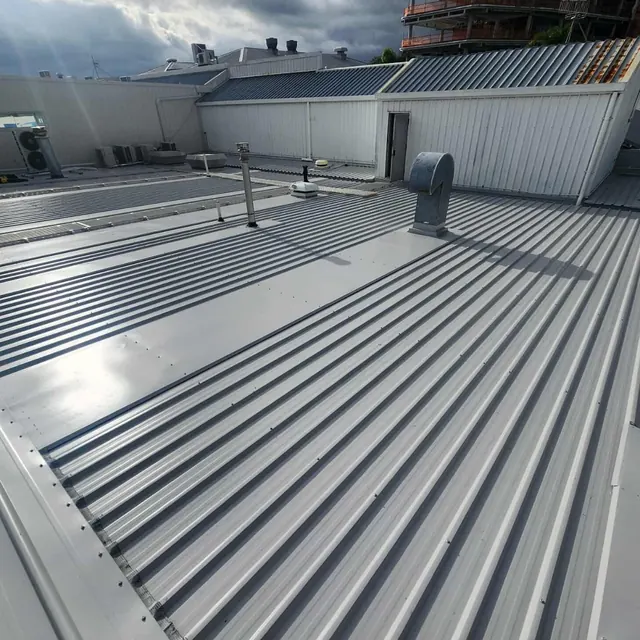 Large commercial re-roof showing new metal roofing, internal gutter details, and rooftop ventilation by ADCO Roofing.