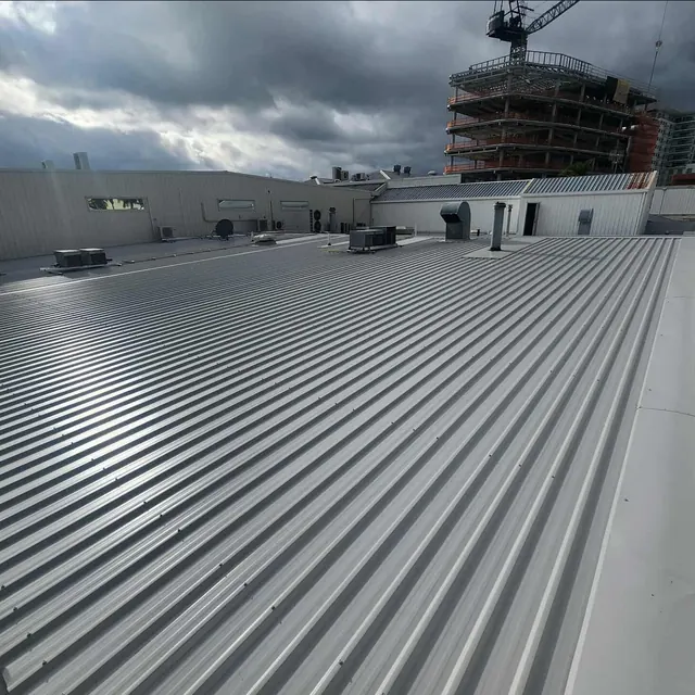 Wide view across a completed commercial metal roof with longrun sheets and city construction in the background.