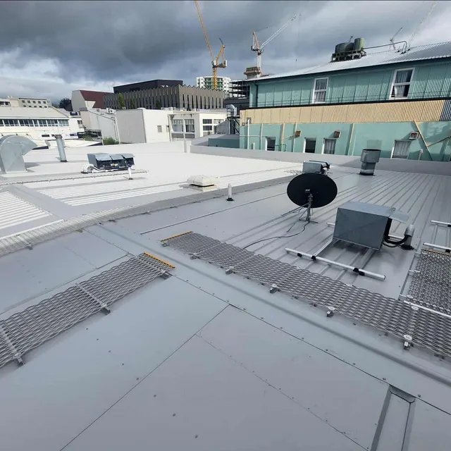Commercial roof conversion with internal gutters, roof access mesh, satellite equipment, and surrounding city buildings.